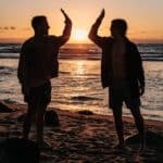 silhouette of two mens near seashore about to high five during sunset